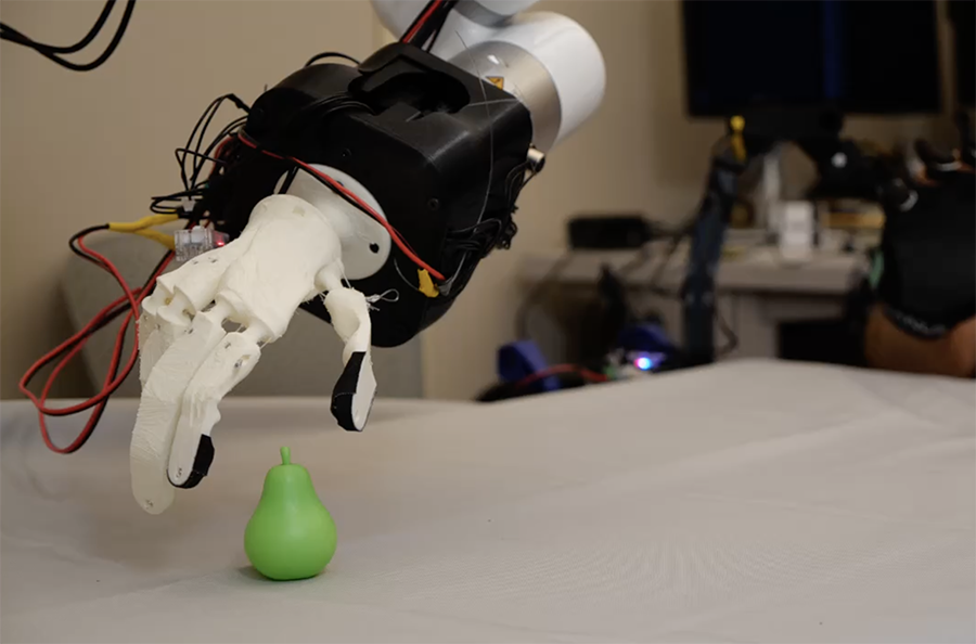 A robotic hand made with a white plastic material reaches out to grasp a green toy pear.